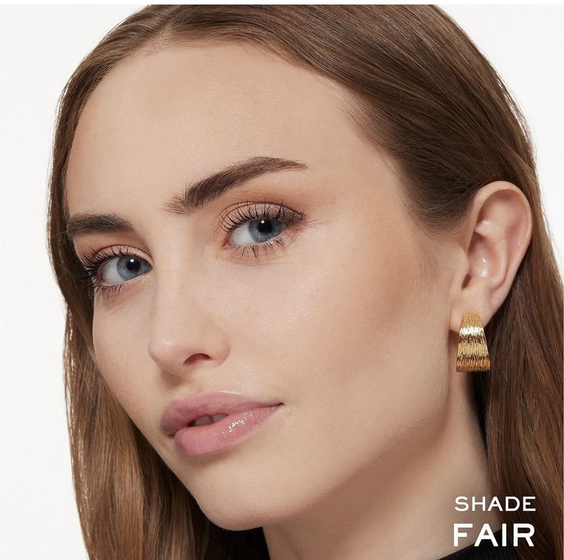 Close-up beauty shot of an adult woman with fair skin, wearing gold earrings, against a neutral backdrop, showcasing beauty and fashion.