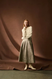 Model wearing white knit sweater and metallic skirt against warm brown backdrop for ME+EM October 2 lookbook