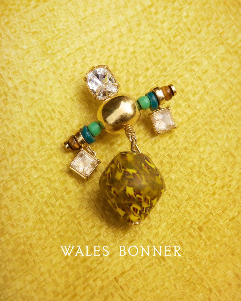 Detailed shot of an ornamental pin featuring an array of beads, gems, and a dangling pendant against a woven yellow surface.