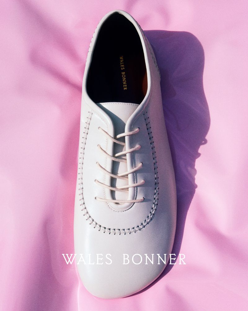 Elevated shot showcases a single, off-white leather dress shoe with matching laces, set against a soft pink fabric backdrop.