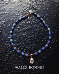 Beaded necklace with blue and brown beads and a crystal pendant on a textured black background for Wales Bonner SS25 Accessories.
