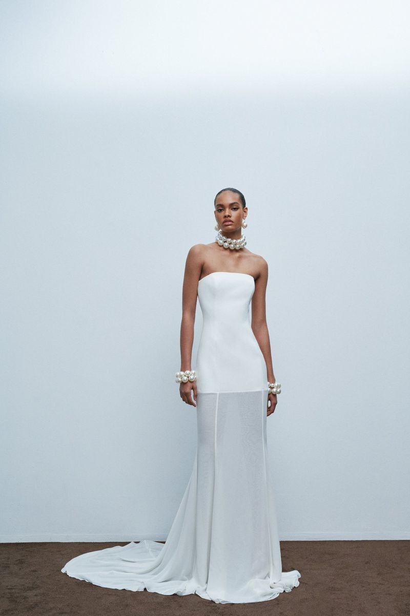 Woman in elegant white strapless gown with pearl jewelry standing in a bright studio. Fashion, beauty and formal wear concept.