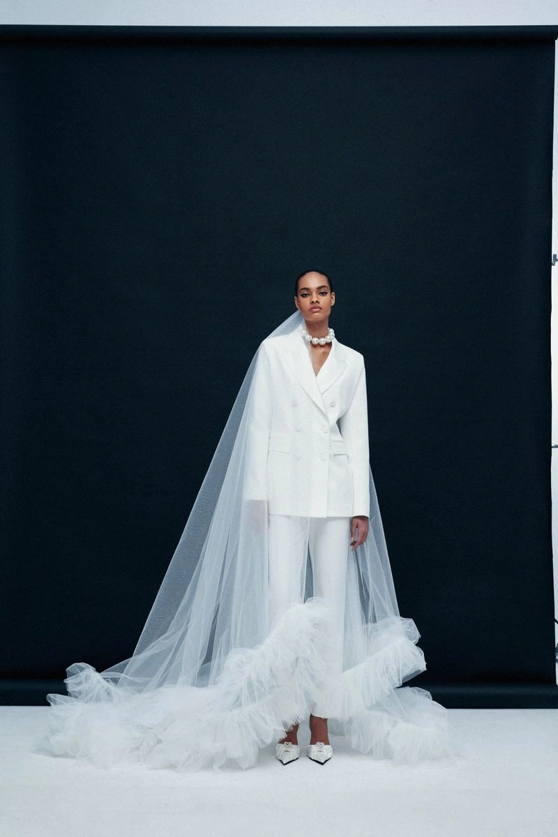 Model in a white bridal pantsuit with a long tulle veil against a dark background
