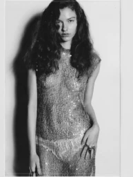 Model with long dark wavy hair wearing a glittering textured dress against a plain background