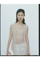 Model in a sheer embellished dress holding a white clutch against a light background for Rachel Comey Resort 25