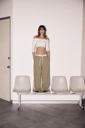 Model standing on a waiting room chair wearing an off-shoulder white crop top and beige trousers for Zara.