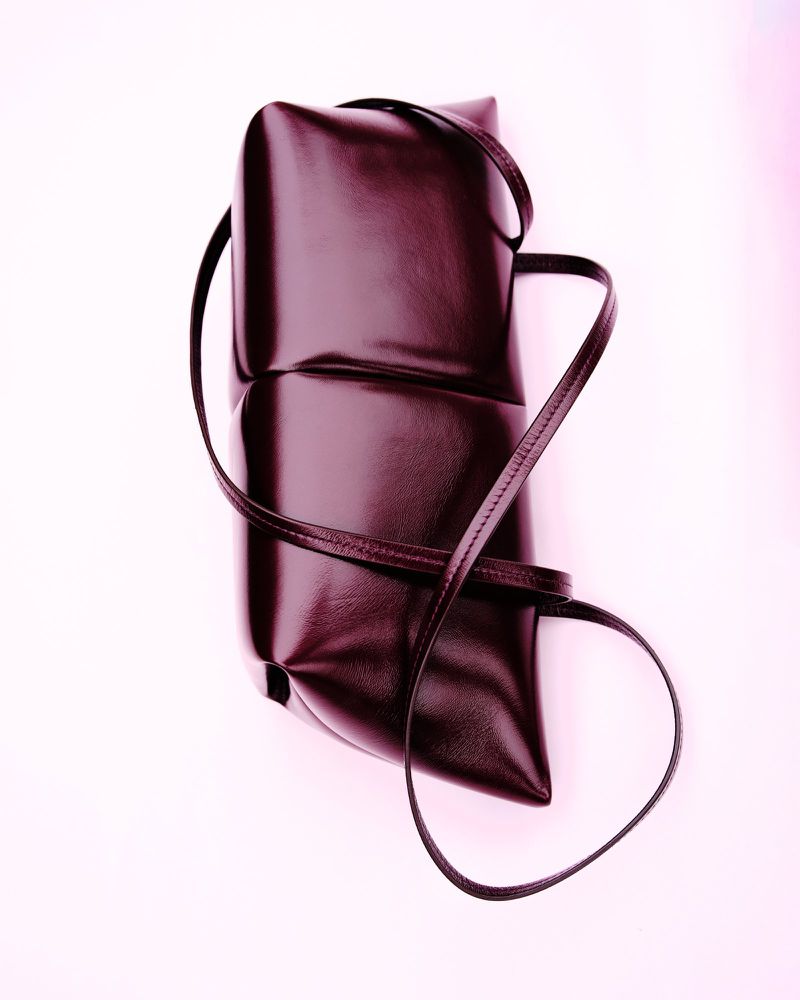 Burgundy leather shoulder bag with a soft, rounded geometric shape and thin strap, set against a clean, light background.