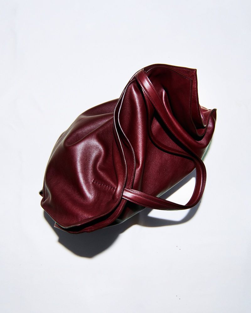 Burgundy leather tote bag with a slouchy design and loop handles, presented on a stark white backdrop with cast shadows.