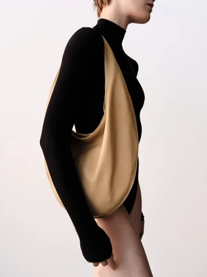 Model wearing black top and carrying tan leather shoulder bag against white seamless background