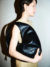Model wearing a light dress holding a large black leather handbag against a plain wall with a sharp shadow