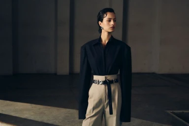Model in oversized black shirt and beige high-waisted trousers with statement belt in an architectural interior