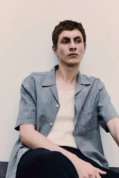 Model wearing a blue button-down shirt and light top against a plain studio background