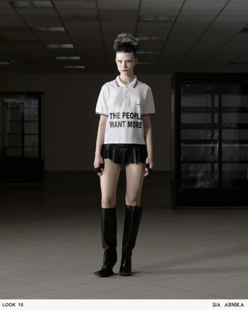 Fashion shot of a slender adult female wearing a white polo shirt with black trim, a black skirt, and black boots in an empty space.