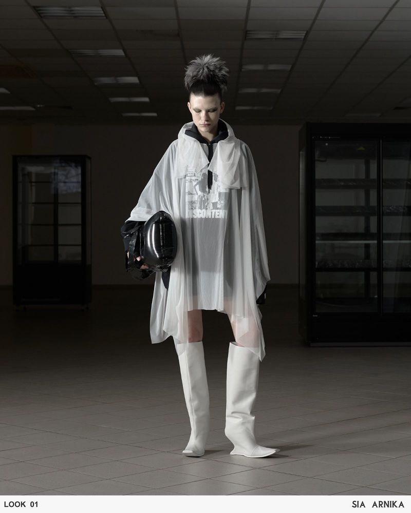 A fashion shot presents a model in a hooded cape, accessorized with white boots and a glossy helmet, set against a muted, dark indoor backdrop.