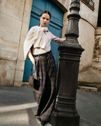 Model standing next to an ornate iron lamppost in front of a blue double door wearing a cream sweater and plaid trousers.