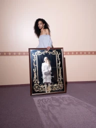 Model with long dark hair holding an ornate framed mirror reflecting another model in white clothing.