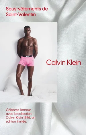 A Black man standing against a white studio background wearing pink Calvin Klein boxer briefs with branded waistband
