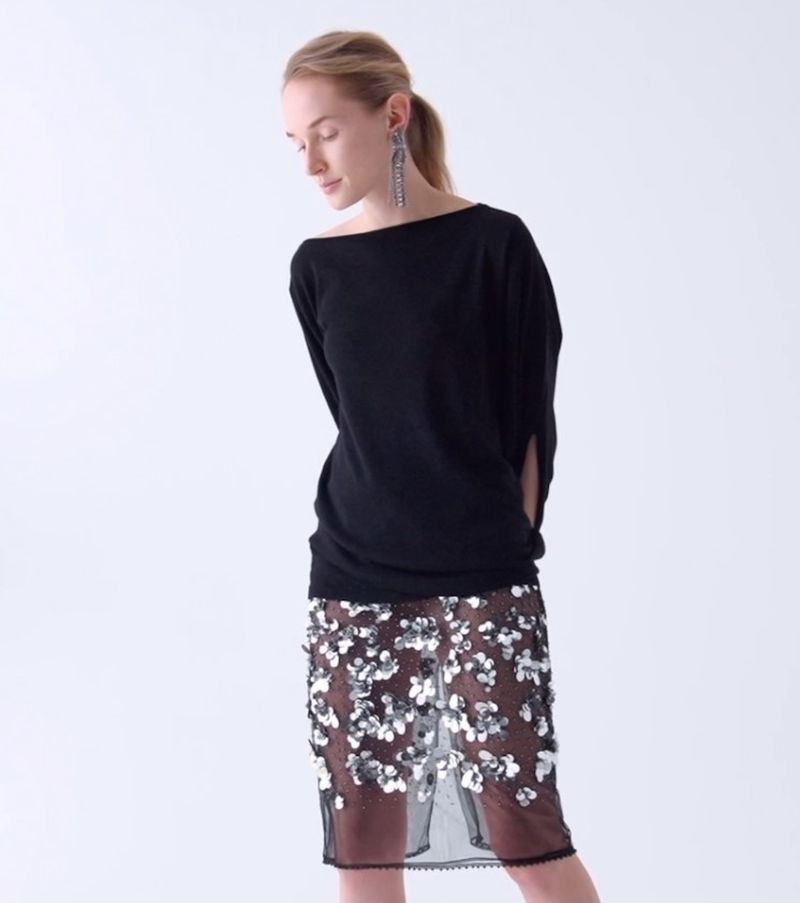 Blond woman poses in a black top and a floral sequined skirt in a studio, creating a fashion editorial image with soft lighting.