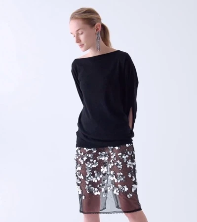 Blond woman poses in a black top and a floral sequined skirt in a studio, creating a fashion editorial image with soft lighting.