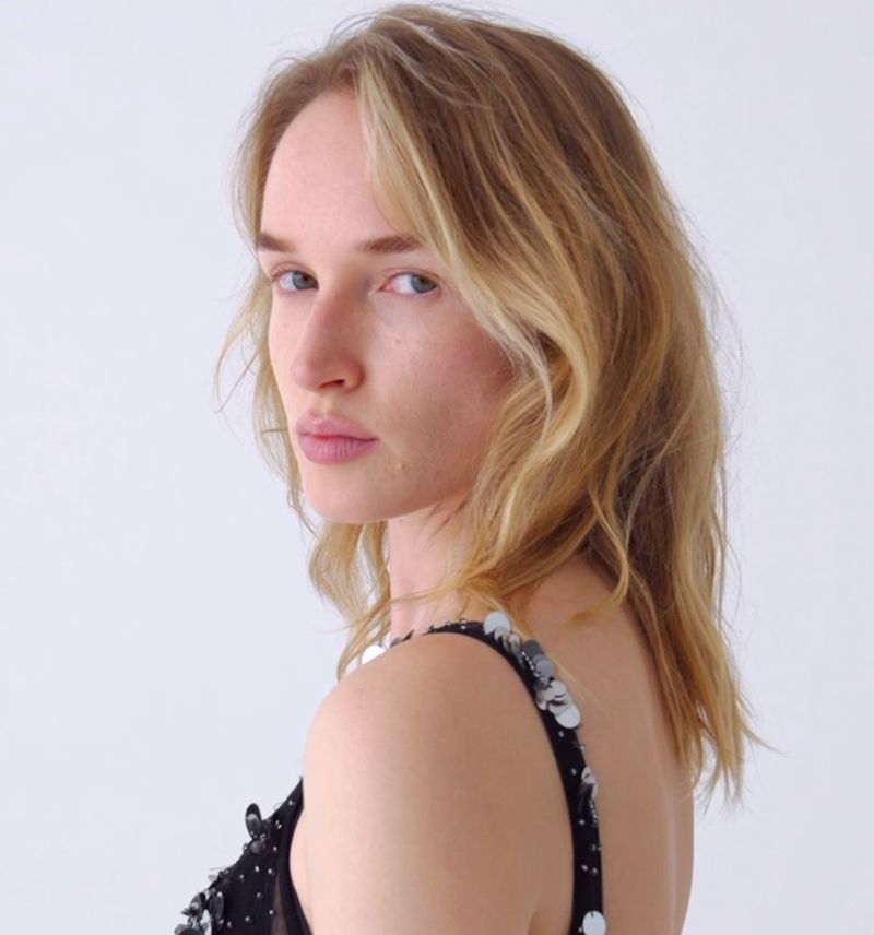 Portrait of a young adult woman with blond hair looking over her shoulder against a white background in a fashion forward setting.