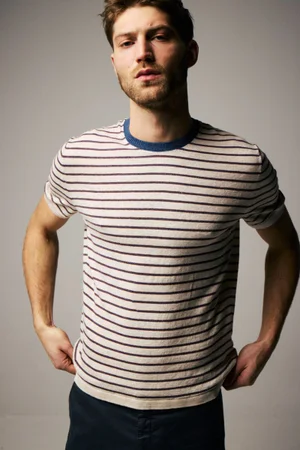 Model Boyd Gates posing in a striped short-sleeve knit shirt and dark trousers against a neutral studio backdrop.