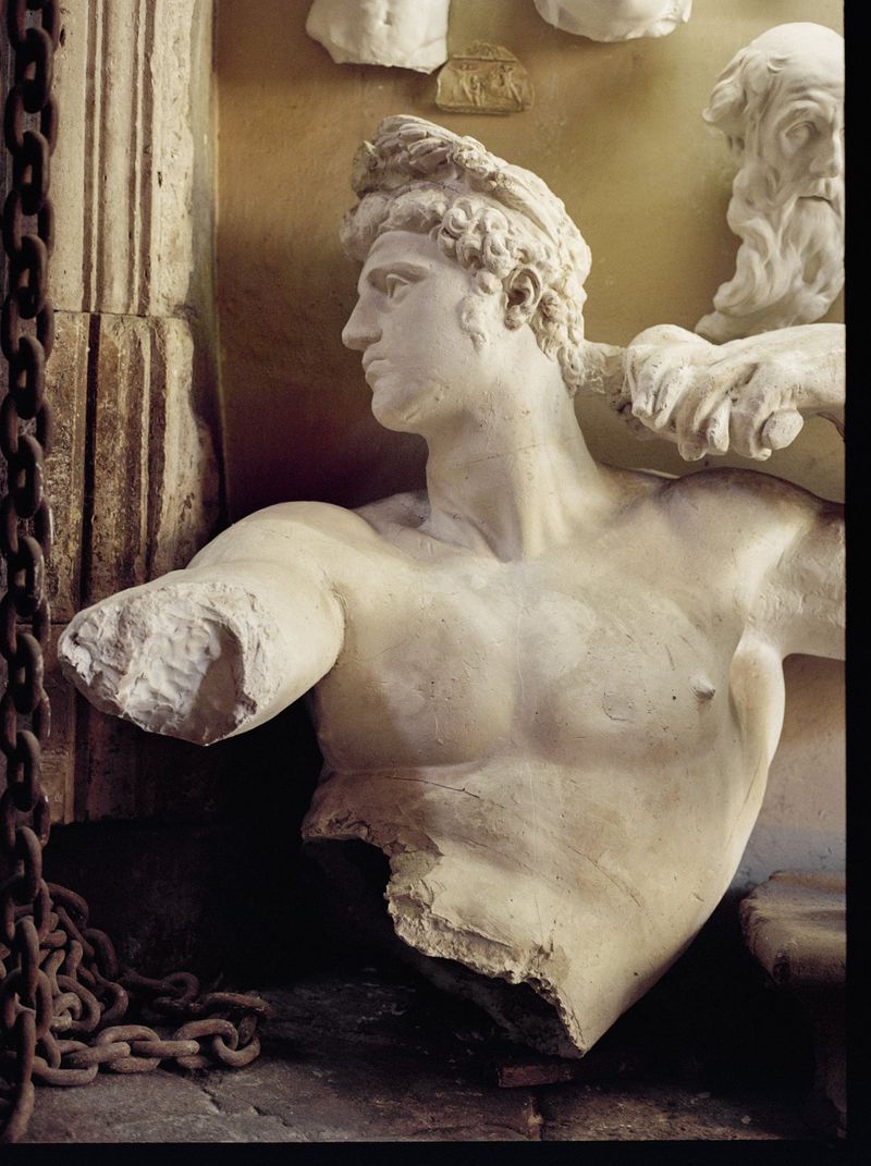 Fragment of a Greco-Roman style marble statue with a partially destroyed torso, displaying classical era artistic style indoors.