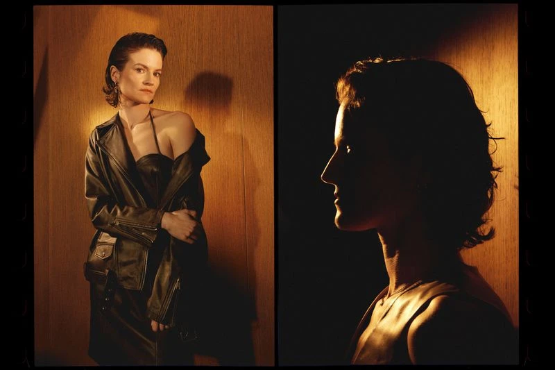 Portrait of an adult woman in a black leather jacket and dress, against a wood-paneled wall; a second profile view is silhouetted.