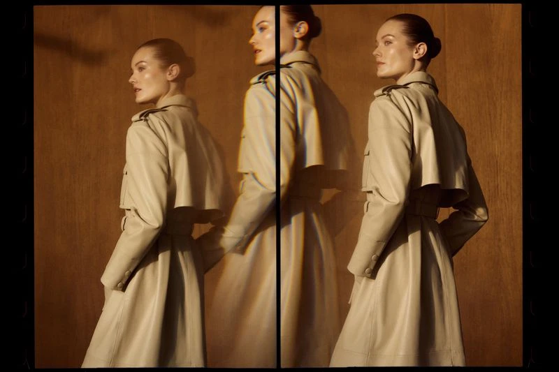 A woman in a tan trench coat poses in a studio, viewed from the side with a blurred triple exposure effect. Fashionable studio shot.