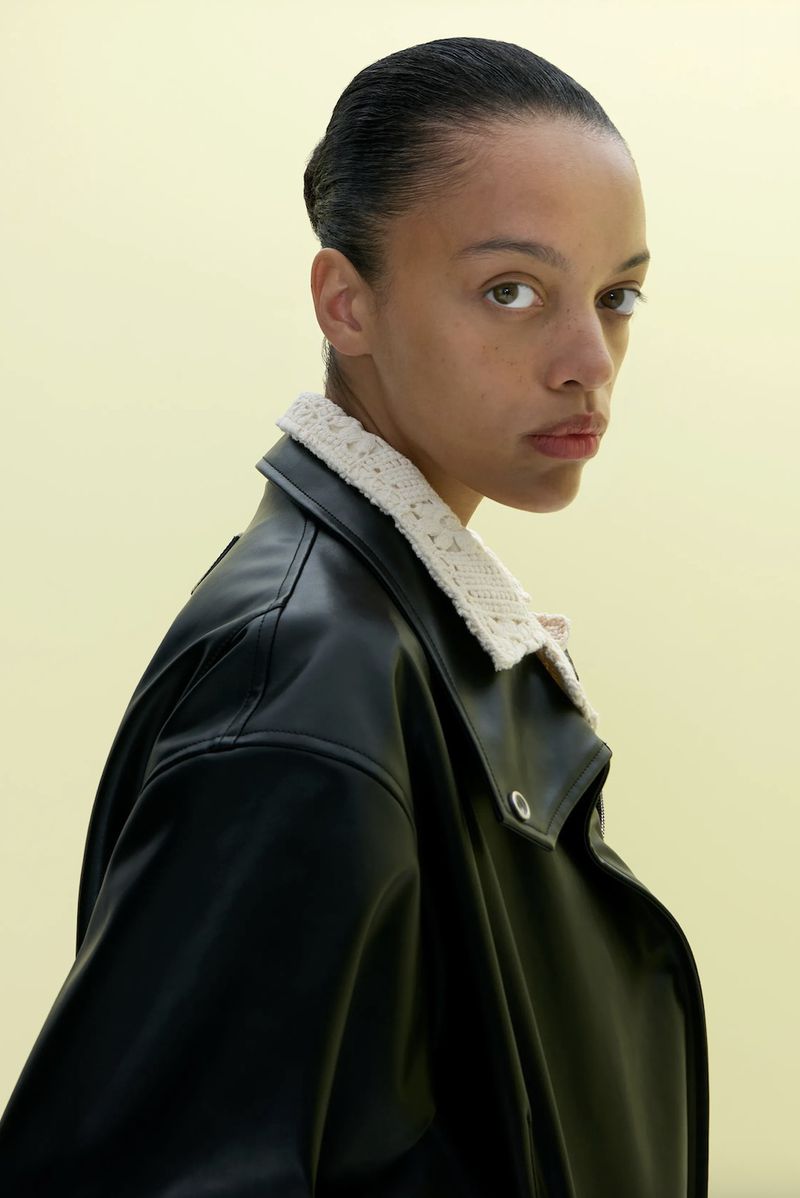 Fashionable Black woman poses in a black leather jacket with knit collar, shot indoors under studio lighting. Beauty and fashion concept.