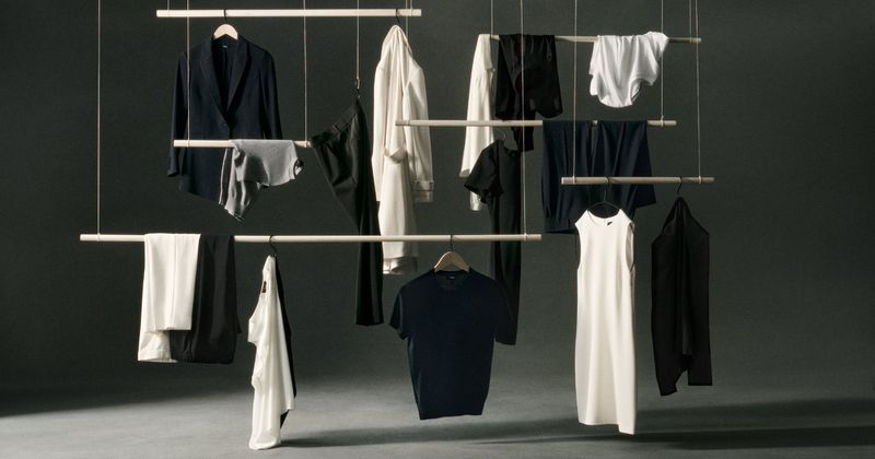 Arrangement of dark and white clothing hanging on wooden racks against a dark gray background, studio lighting, simple aesthetic.
