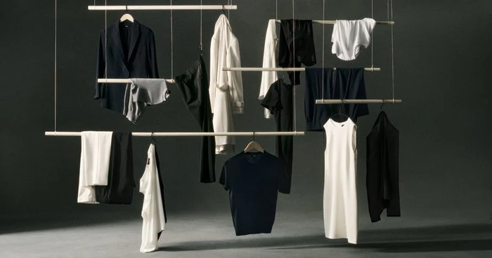 Hanging garments on wooden bars suspended by strings against a dark studio background for Theory Wardrobe 2024