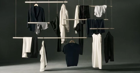 Hanging garments on wooden bars suspended by strings against a dark studio background for Theory Wardrobe 2024