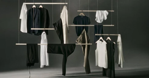 Suspended garments on wooden hangers and rods floating against a minimal dark grey studio background.
