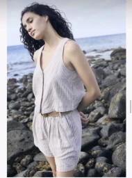 Evelina Sakalauskaite wearing a striped linen vest and matching shorts on a rocky coastline.