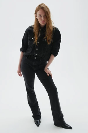 Model wearing a black denim jacket and matching flared jeans with pointed black boots against a white studio background.