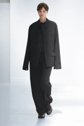 Model wearing a black jacket and matching trousers walking against a bright white background
