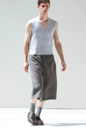 Male model wearing a pale blue v-neck vest and dark grey shorts against a plain white studio background.