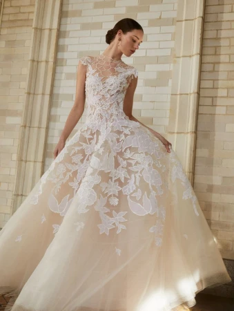 Elegant woman in a light peach ballgown with lace floral details, posing in an indoor setting with natural light.