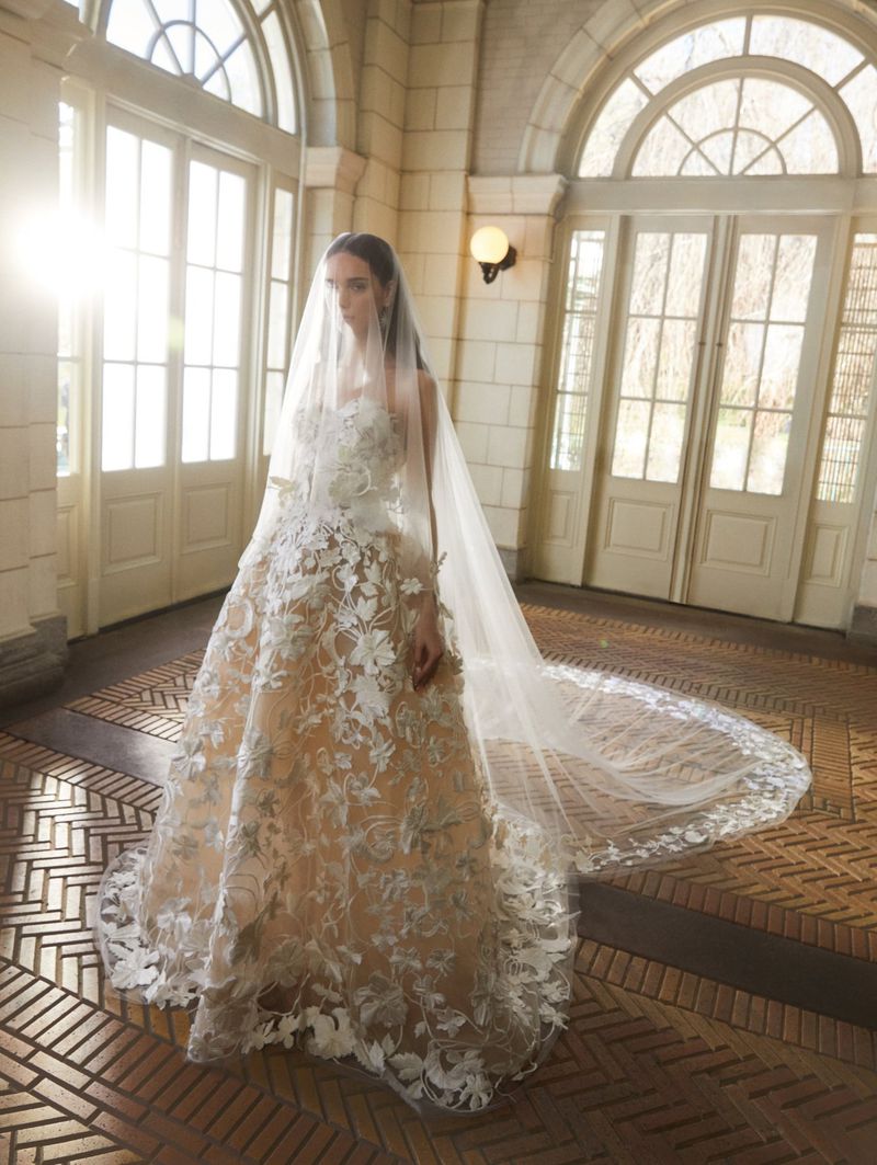 Elegant woman in a wedding dress with a long veil stands inside a building with arched doorways and windows, creating a bright and airy atmosphere.
