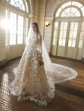 Elegant woman in a wedding dress with a long veil stands inside a building with arched doorways and windows, creating a bright and airy atmosphere.