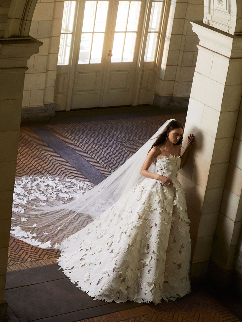 Woman poses in a white strapless wedding dress with butterfly accents and a long veil in an indoor hallway with stone pillars.