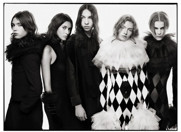 Five models in dark and harlequin patterned outfits standing against a plain white studio background.