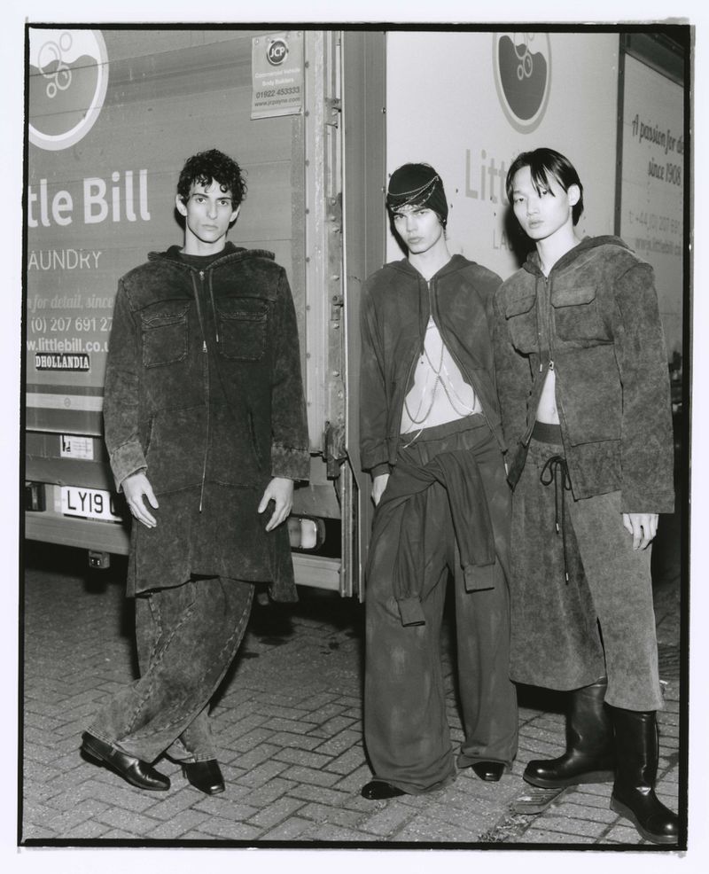 Three young male fashion models pose in matching outfits outside a Little Bill Laundry truck in a monochromatic fashion editorial.