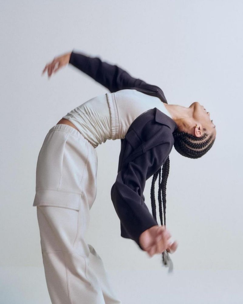 Woman in active pose wearing casual jacket, white top, and cream-colored cargo pants against plain backdrop in studio setting.