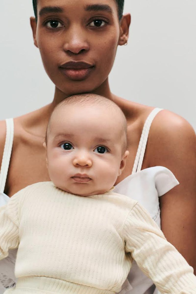 Close-up of a woman holding a baby in her arms. The image features natural light and a soft color palette, highlighting the subjects.