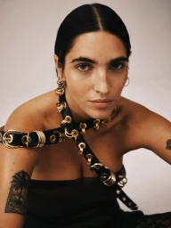 Model Valentine Valero wearing a black leather belt with gold metal eyelets wrapped around her torso against a studio backdrop.