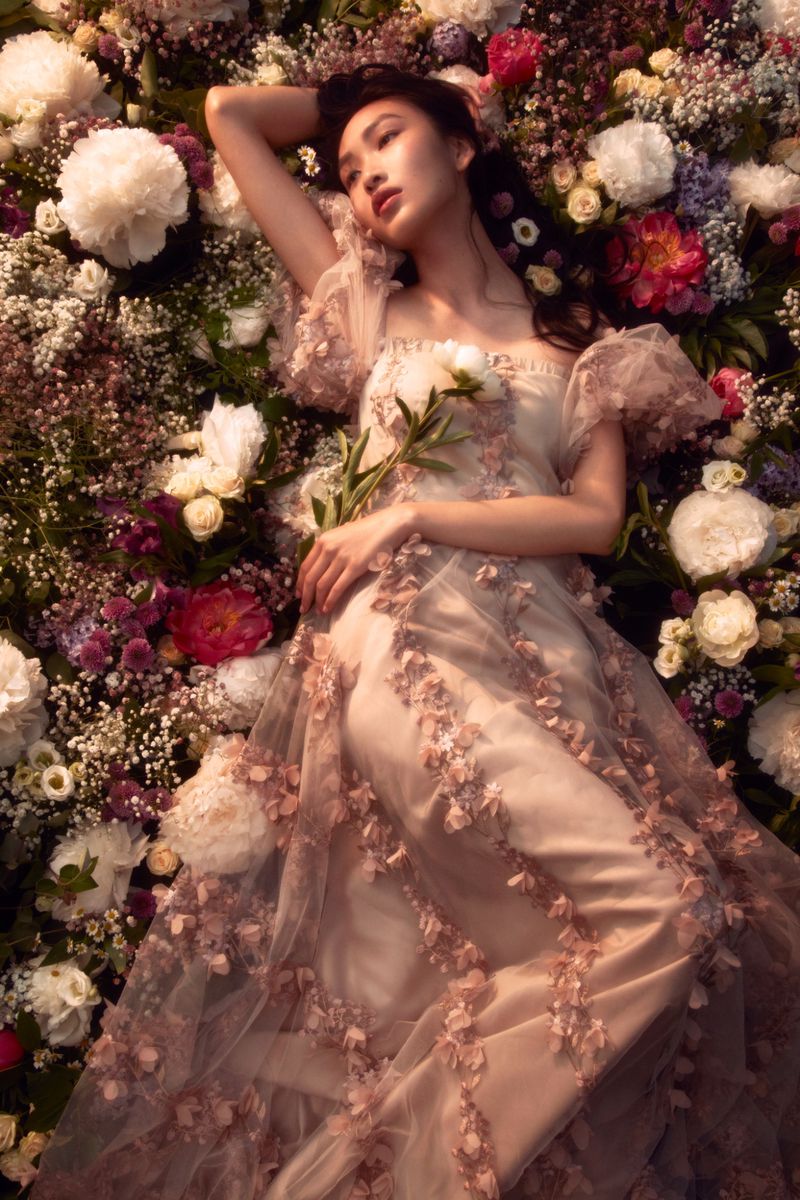 An Asian woman in an elegant dress lies among a vibrant array of flowers, exuding a serene and dreamlike aesthetic.