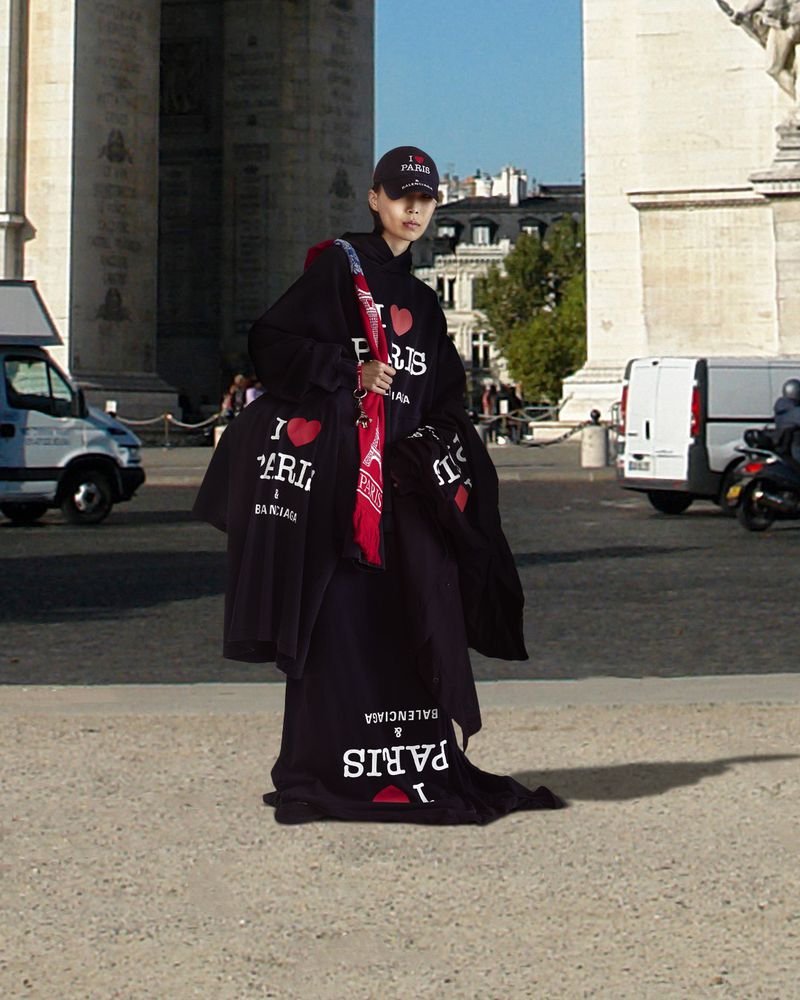 Fashionable adult in streetwear poses near the Arc de Triomphe in Paris, France. The individual wears clothing with "I ❤️ Paris" text.