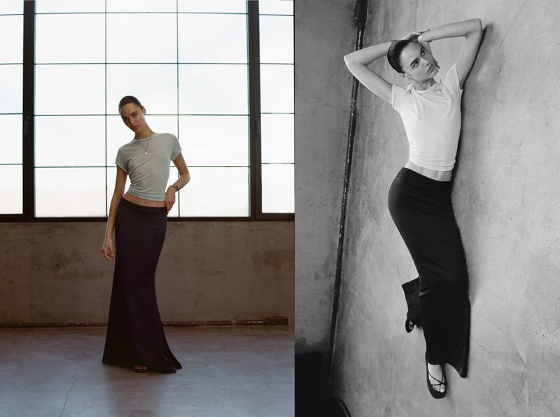 Fashion shot featuring a young adult female model posing in a light blue shirt and black skirt, standing in an indoor industrial space.