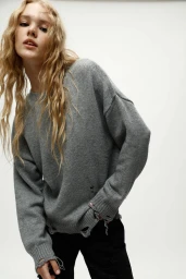 Model in a distressed grey knit sweater and black trousers against a plain white background for Lefties